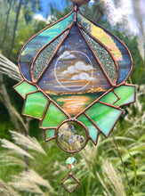 Load image into Gallery viewer, Gouache landscape set between glass with pressed forget-me-not flowers. Iridescent purple and textured clear glass border with green crystal formation. Hanging iridescent bevel and clear diamond glass bevel.
