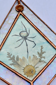 Spider with miniature landscape in body above pressed daisy flower and fern painted with gouache on paper set between glass. Iridescent floral textured glass border and yellow gem.