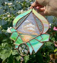 Load image into Gallery viewer, Gouache landscape set between glass with pressed forget-me-not flowers. Iridescent purple and textured clear glass border with green crystal formation. Found word poetry on backside. Wired at top to hang on wall.
